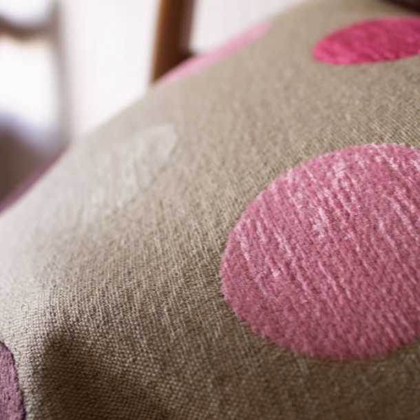 Bonito cojín decorado con topos de colores, tejidos en tonos rosas, sobre un fondo liso color natural.