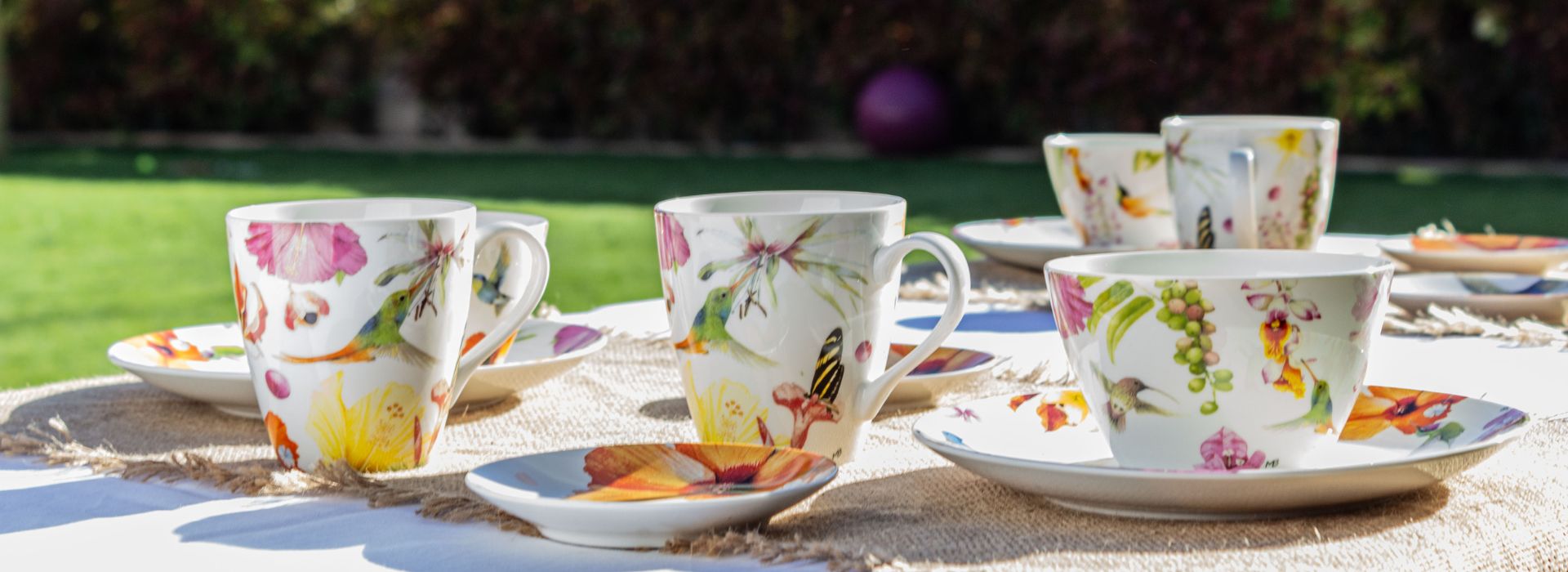 mesa de jardín con tazas y platos de porcelana blanca estampada con colibrís y flores de colores